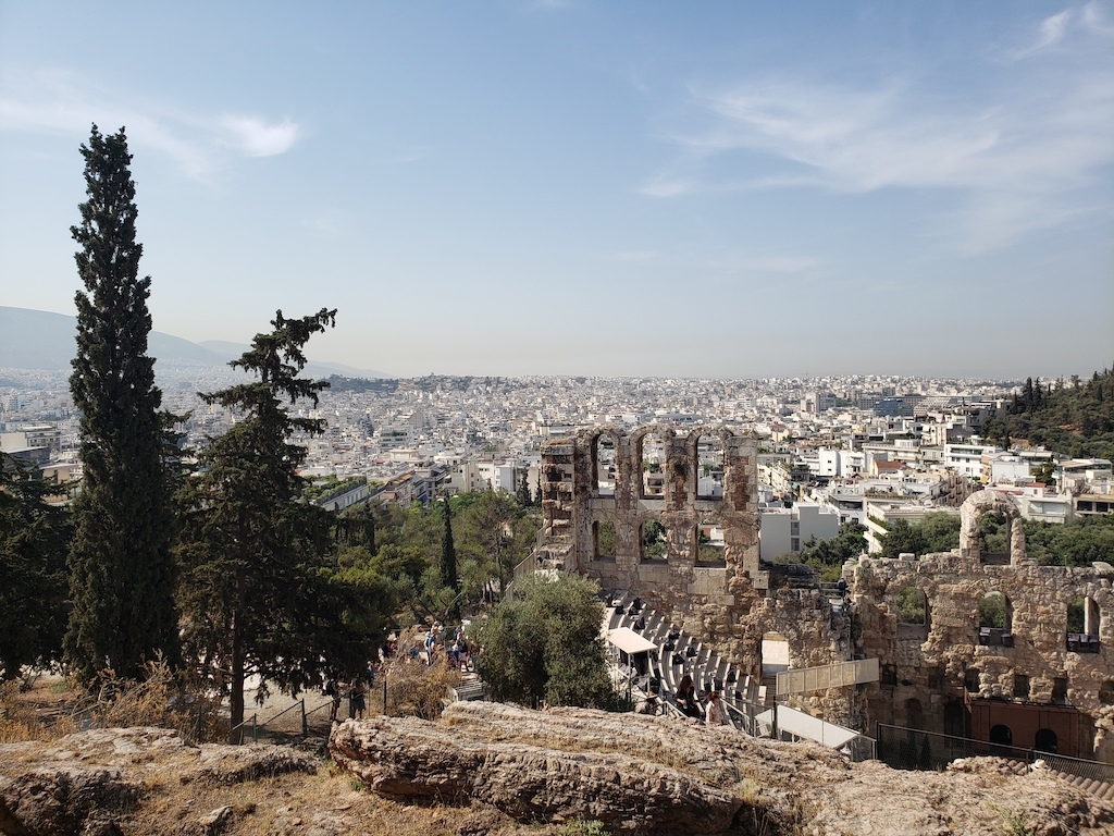 Daytime photo of Grecian ruins overlooking a city in the distance